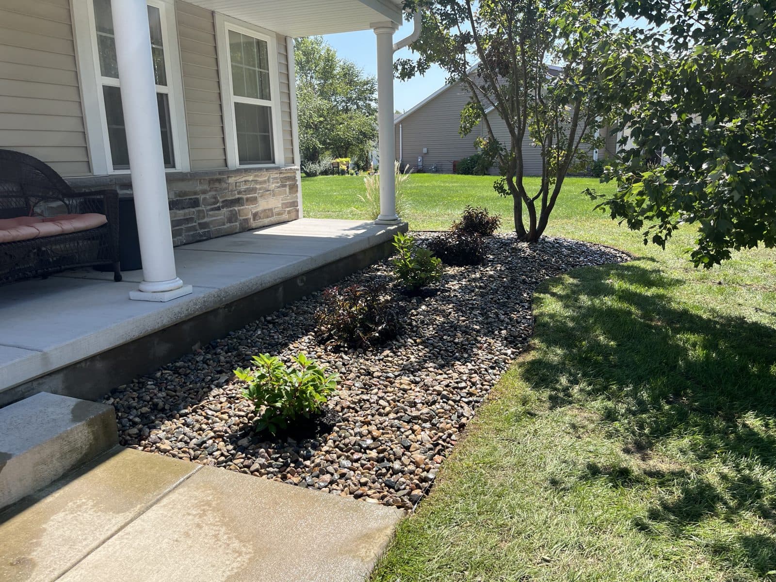 Stone-column front porch with a fresh river-rock bed and walkway plantings by Meeks Mowing & Landscaping